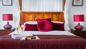 A bedroom with a wooden headboard, a canopy bed, red pillows, and two bedside tables with lamps. - The Claremont (Hove)