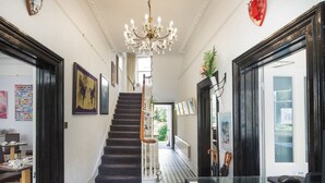 A hallway with a black and white checkered floor, a staircase, and a chandelier. - The Claremont (Hove)