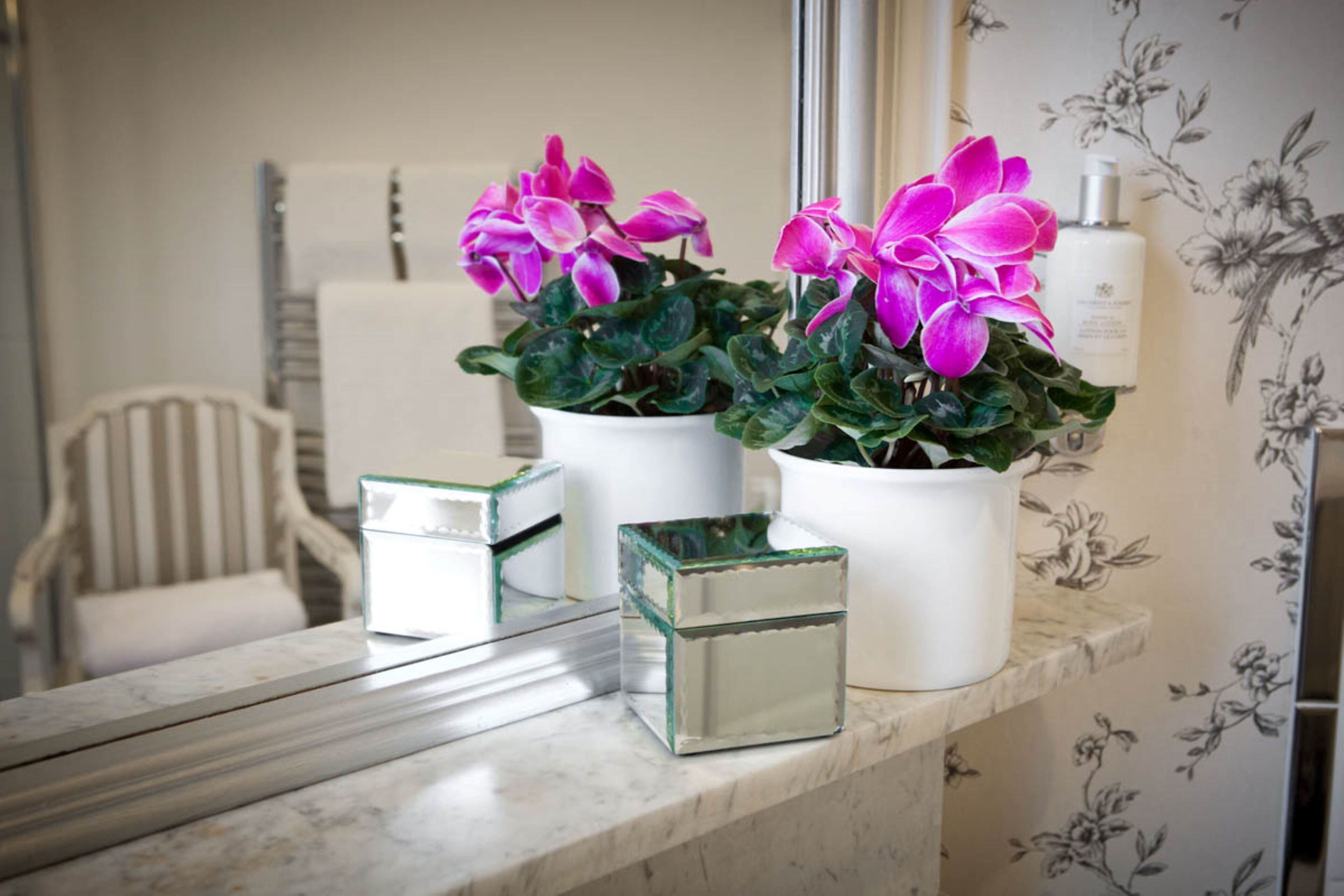 A bathroom vanity with a white marble countertop, two white ceramic flower pots with pink flowers, and a small glass container.