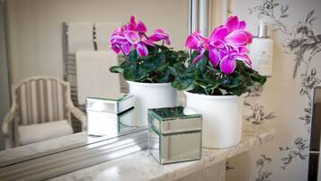 A bathroom vanity with a white marble countertop, two white ceramic flower pots with pink flowers, and a small glass container.