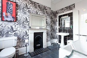 A bathroom with a black and white floral wallpaper, a white toilet, a white sink, a mirror, and a bathtub. - The Claremont (Hove)