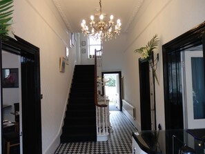 A hallway with a black and white checkered floor, a chandelier, and a staircase leading to another room. - The Claremont (Hove)