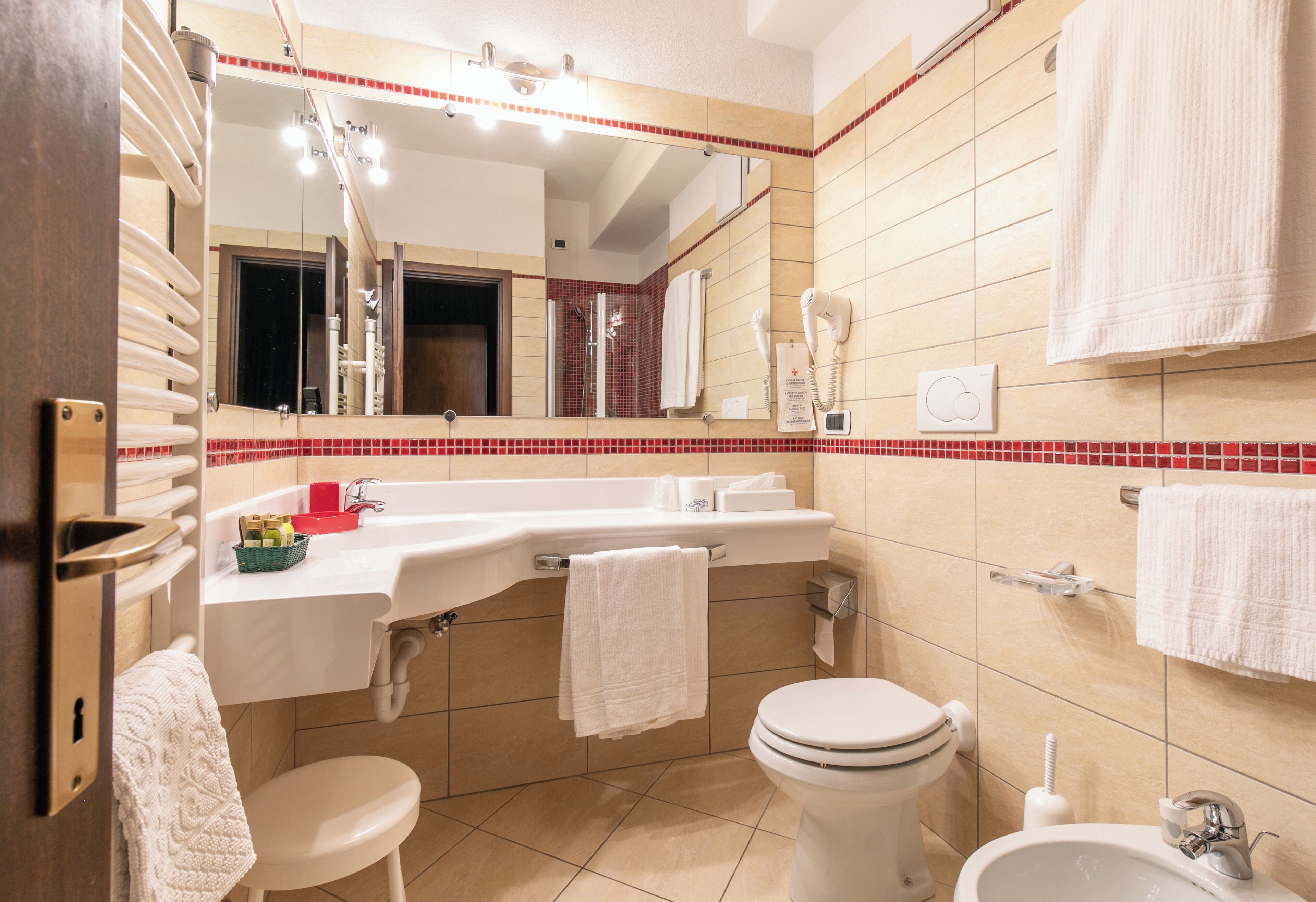 Un bagno moderno con lavandino, vaso e bidet bianchi, uno specchio sopra il lavandino e un porta asciugamani.