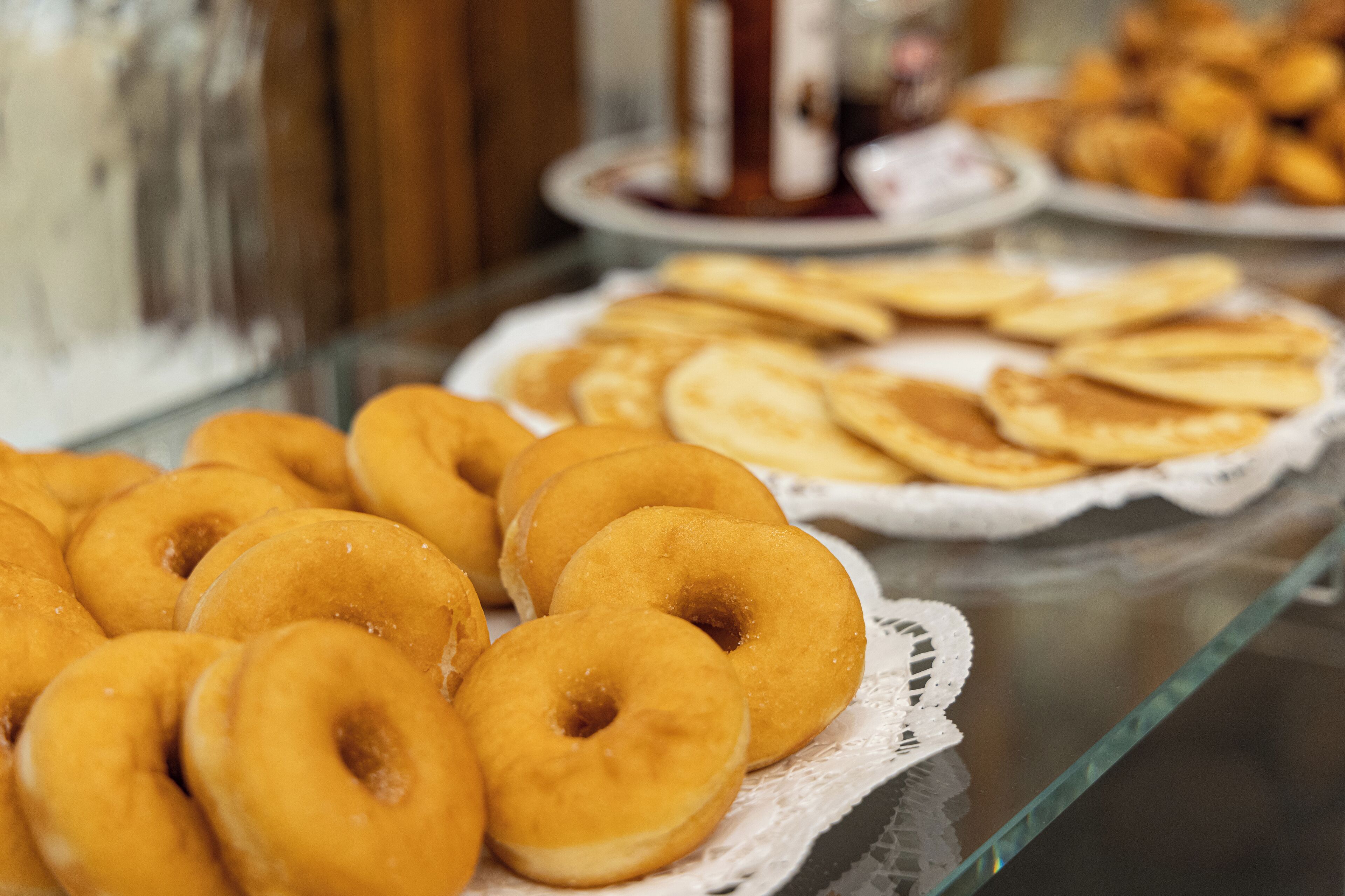 A display of various pastries on a glass counter, including donuts and cookies.