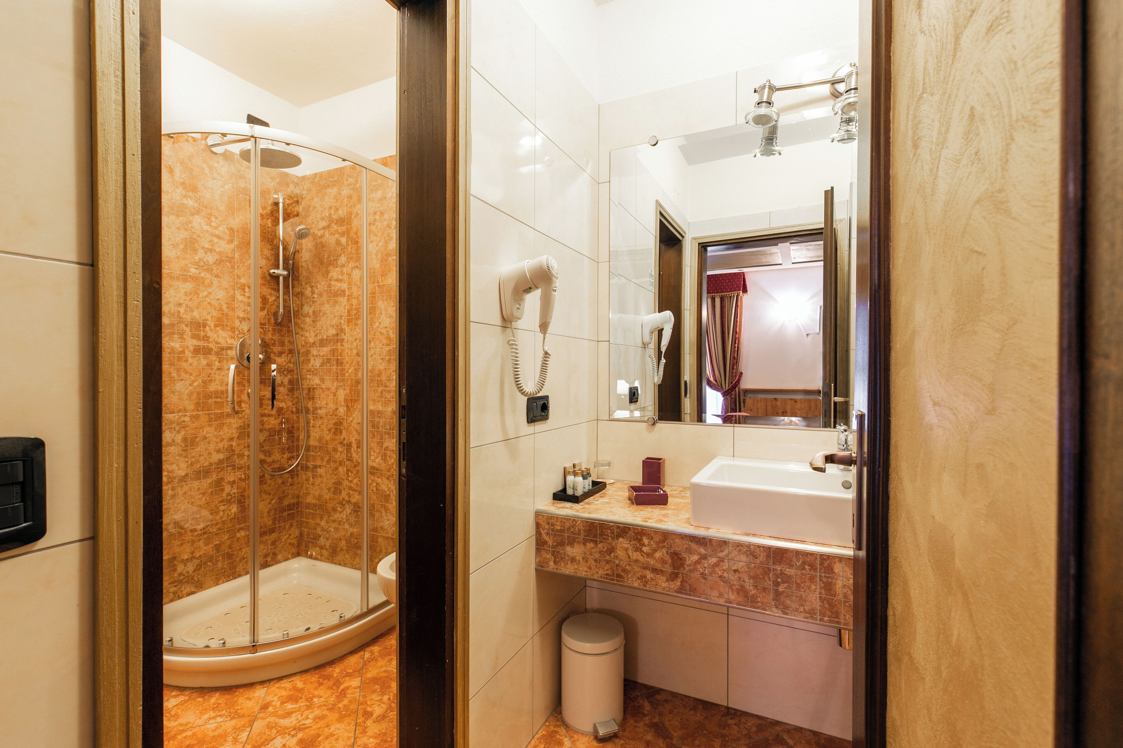 A bathroom with a glass-enclosed shower, a sink with a mirror, and a trash can.