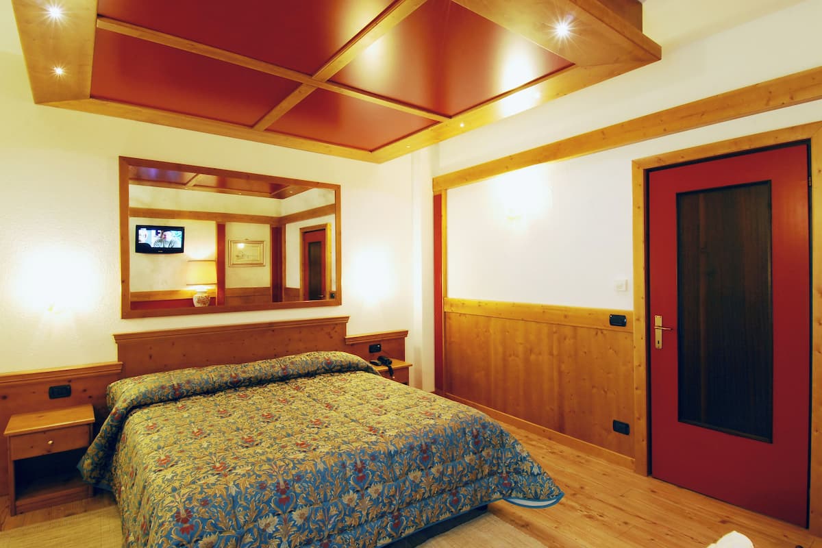 Ein Schlafzimmer mit Holzboden, einem Bett mit blumigem Überwurf, einem Fernseher an der Wand und einer roten Tür.