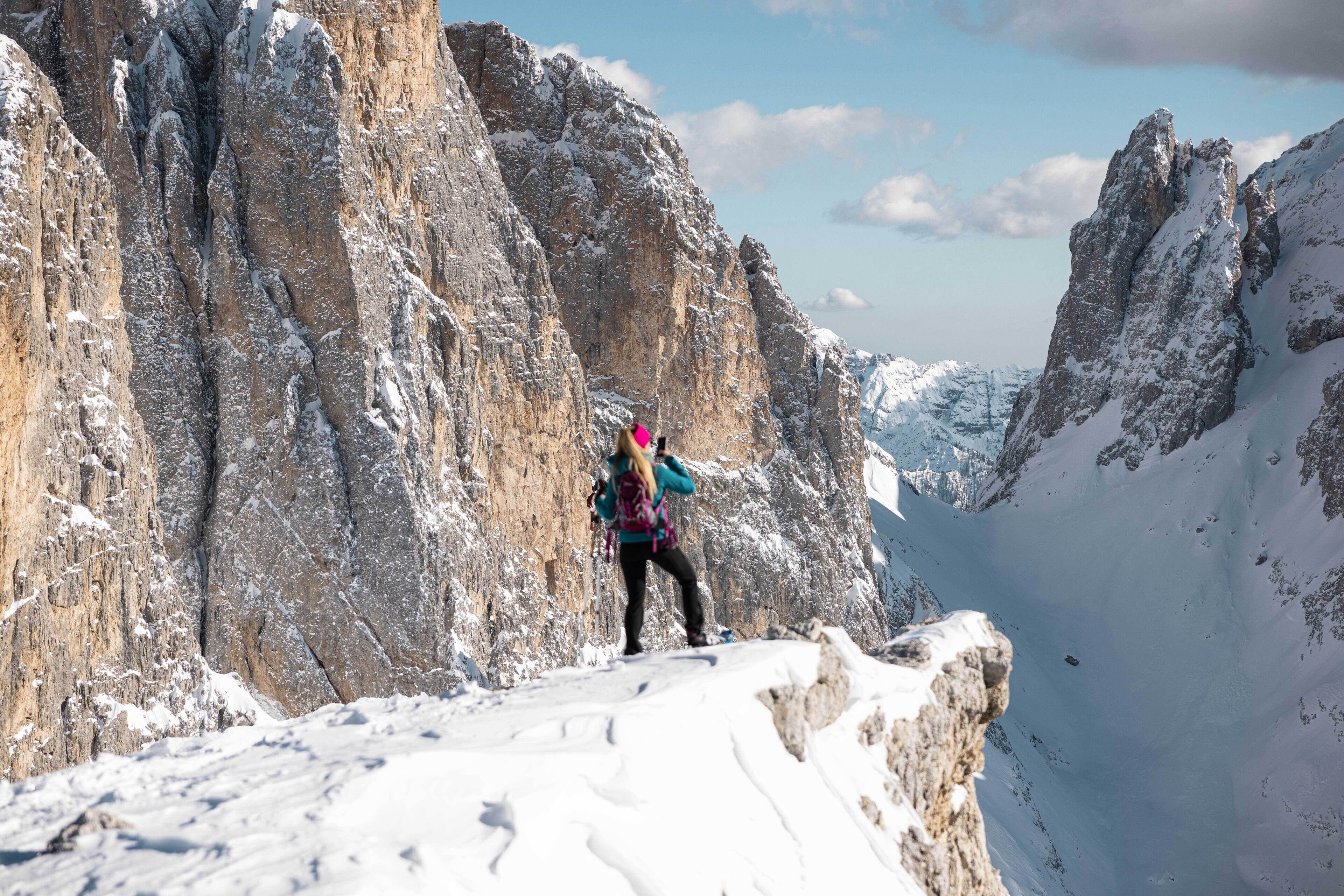 Una persona caminando por un sendero montañoso cubierto de nieve y con acantilados rocosos.