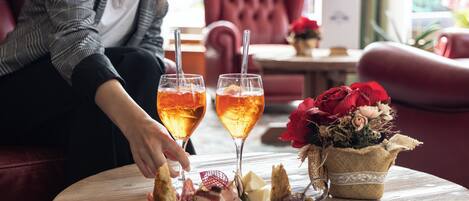 A round wooden table with a charcuterie board, two glasses of a beverage, and a vase of red flowers.