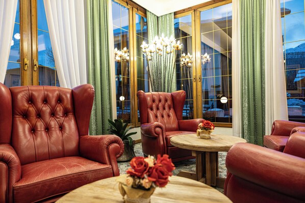 A room with leather armchairs, a round wooden table, and a vase of flowers. - Grand Hotel des Alpes (Primiero San Martino di Castrozza)
