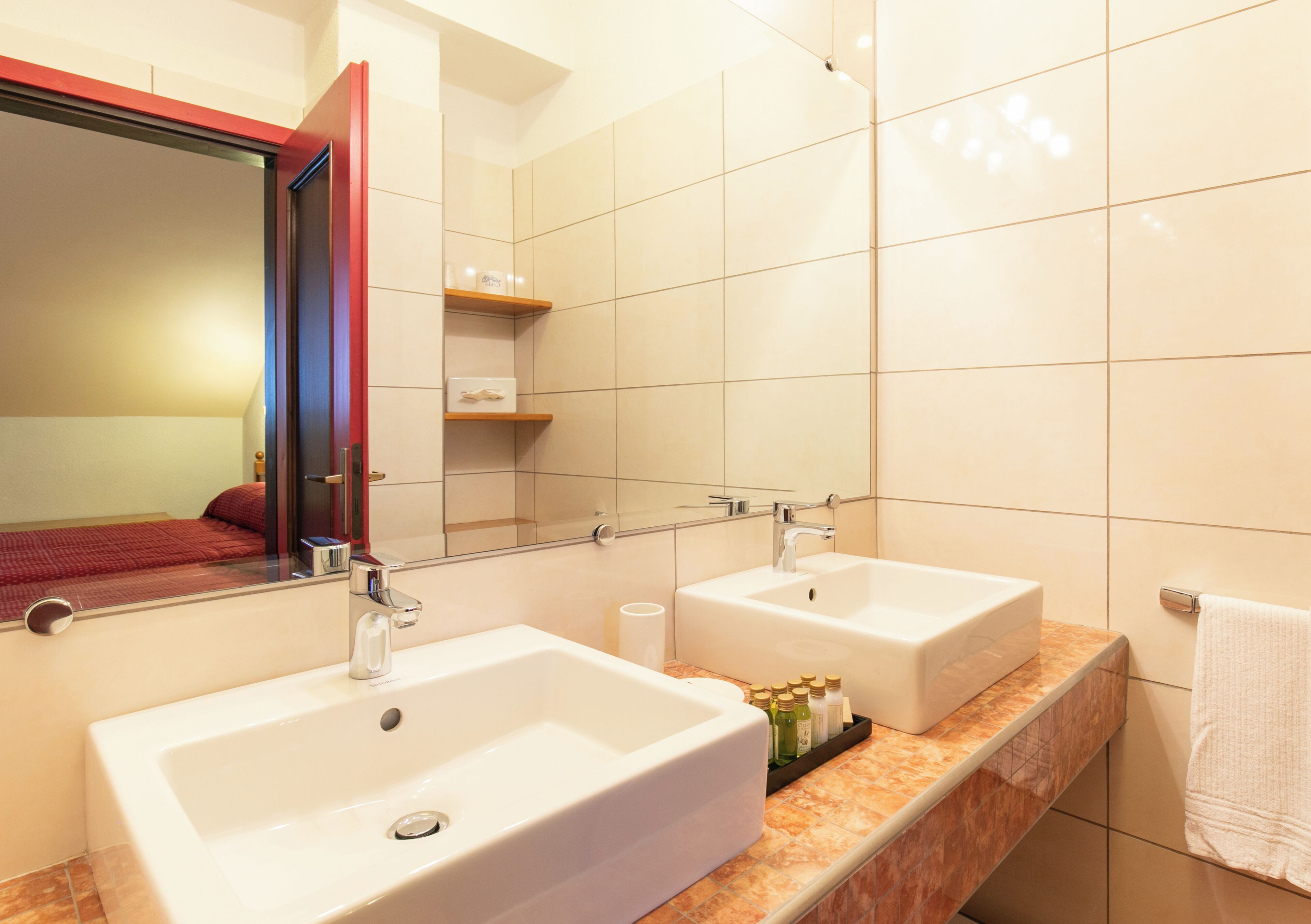 A modern bathroom with two sinks, a large mirror, and a red-framed door.