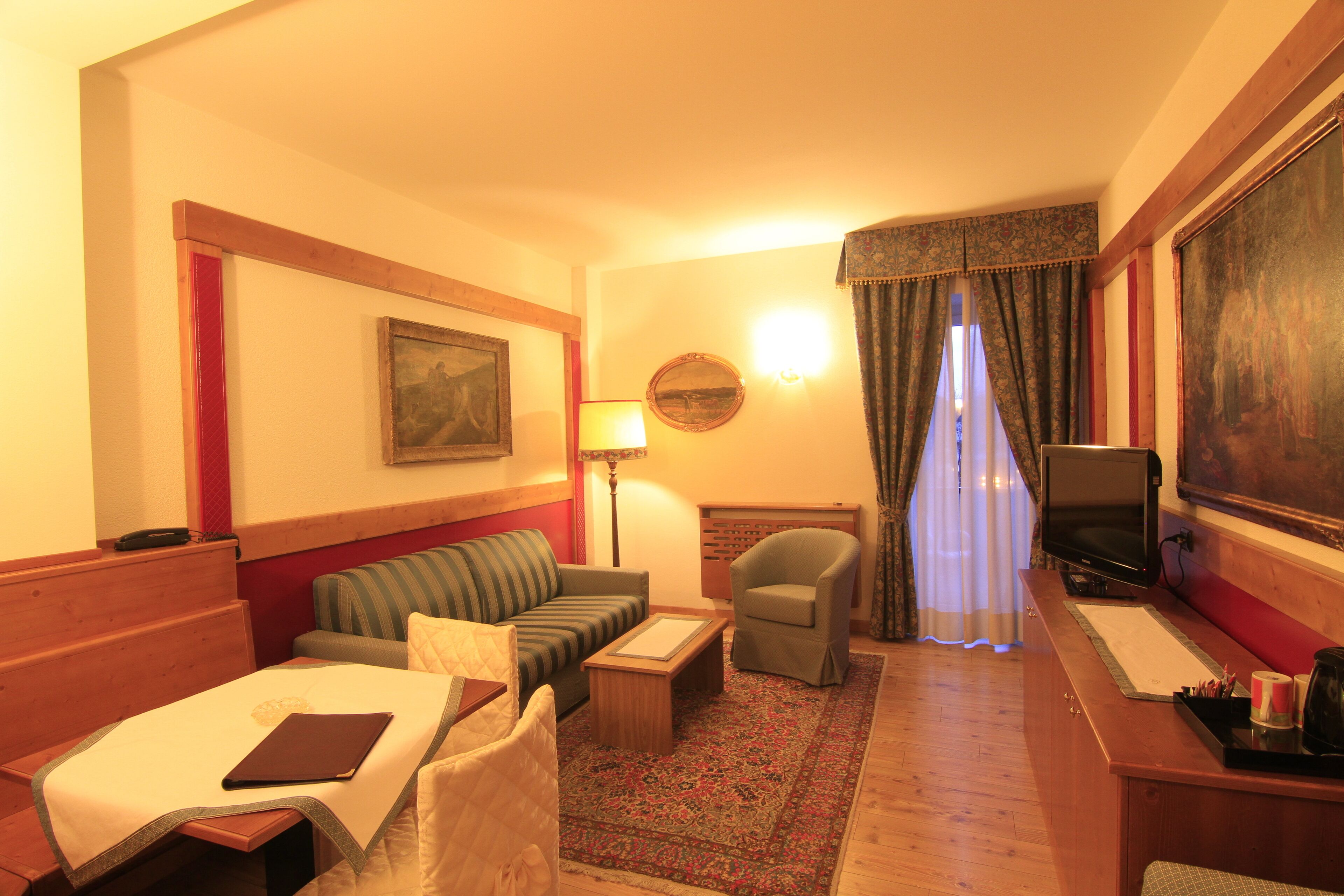 A hotel room with a bed, a sofa, a chair, a desk with a computer, a lamp, and a painting on the wall.