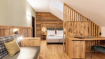 Una stanza accogliente con soffitto in legno, un letto con copriletto a quadri, una poltrona con un cuscino e una scrivania con una sedia.