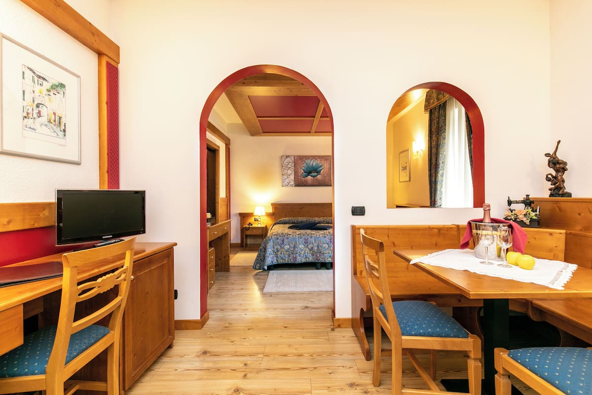 Ein gemütliches Zimmer mit Holzmöbeln, einem Bett mit floralem Überwurf und einem Fernseher auf einer Holzkommode.