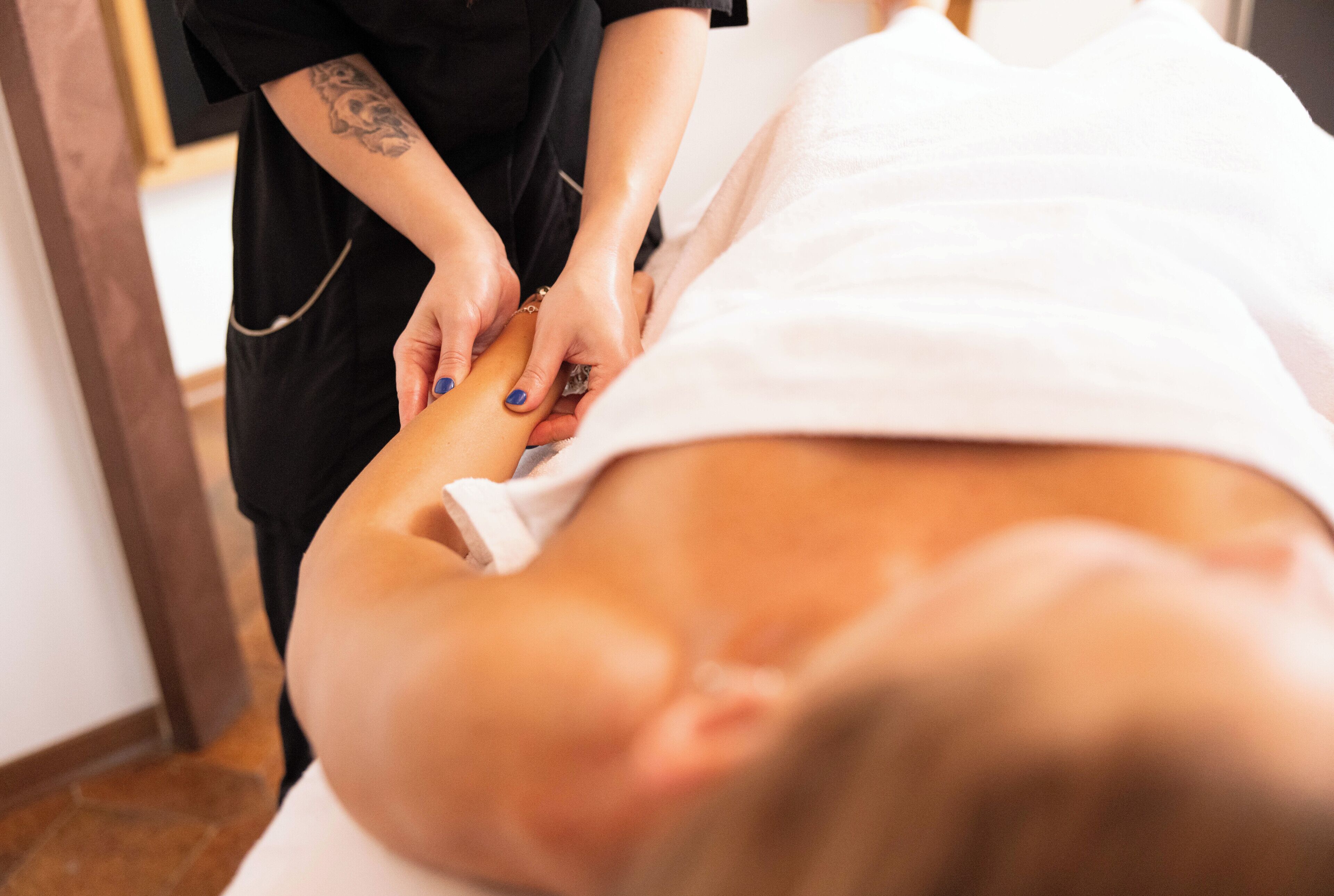 A person receiving a massage in a room with a wooden floor and a white wall.