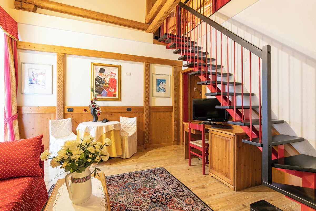 Ein gemütliches Wohnzimmer mit Holzboden, einem roten Sofa, einem Couchtisch mit Blumenvase, einem Fernseher und einer Treppe mit roten Geländern.