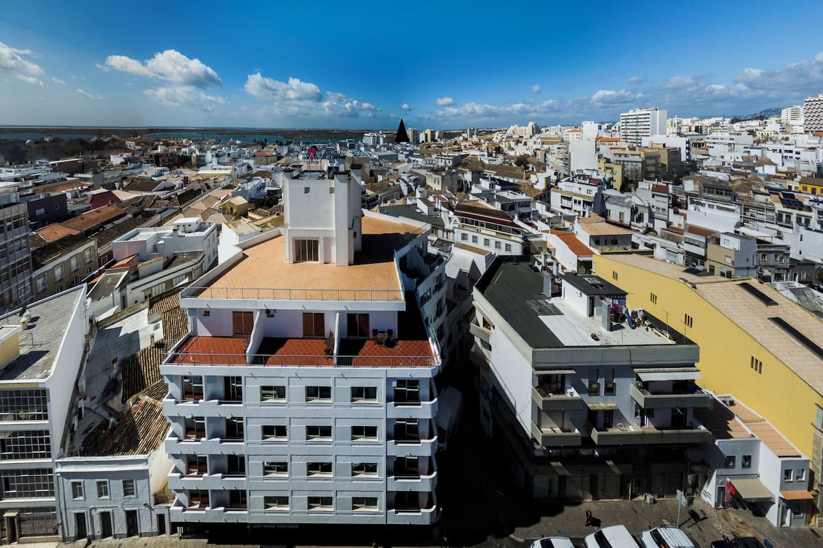 Un edificio alto con varios balcones y un techo de tejas rojas, rodeado por una zona urbana densa con diversos edificios.