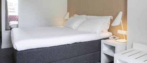A modern hotel room with a large bed, bedside lamps, a nightstand, and a mirror.