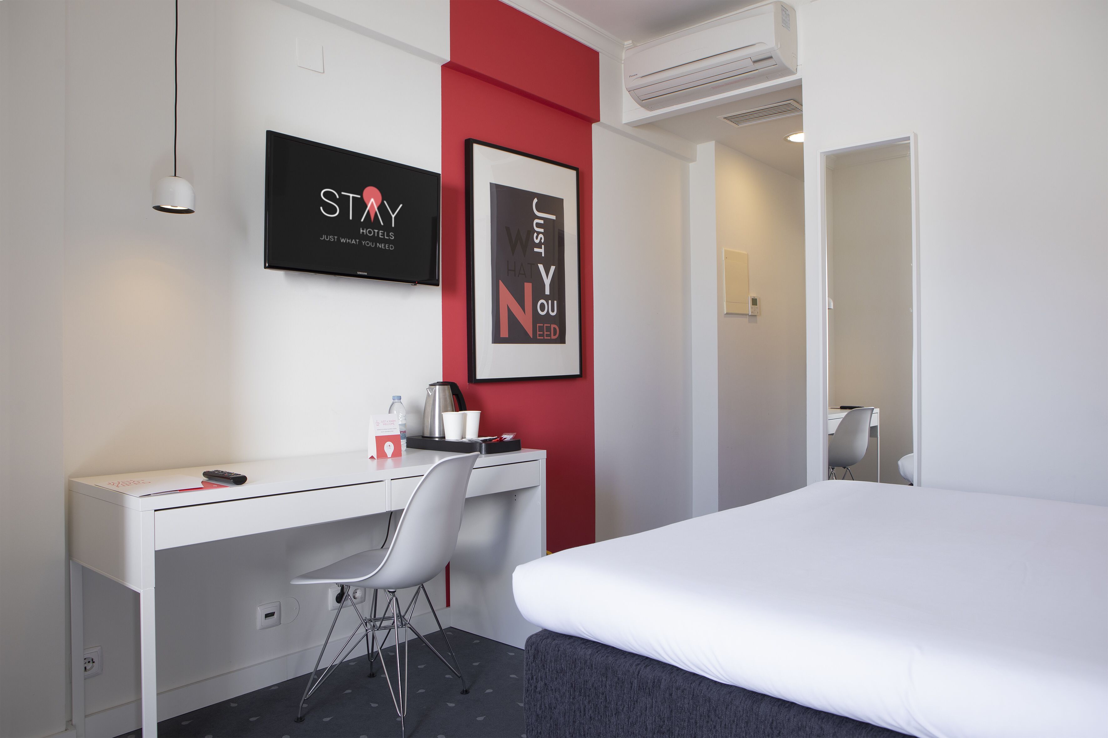 A hotel room with a bed, a desk, a chair, a TV, and two framed pictures on the wall.