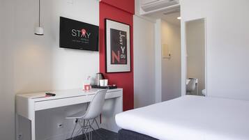 A hotel room with a bed, a desk, a chair, a TV, and two framed pictures on the wall.