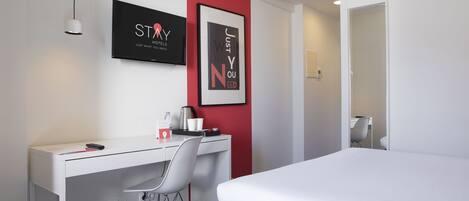 Habitación de hotel con cama, escritorio, silla, televisión y dos cuadros en la pared.