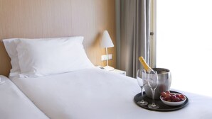 A hotel room with a neatly made bed, a bedside table with a lamp, a bucket with champagne, and a tray with grapes and glasses. - Stay Hotel Faro Centro (Faro)