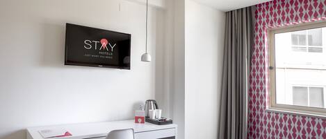 Habitación de hotel con cama, escritorio con silla, televisión y ventana con cortinas.