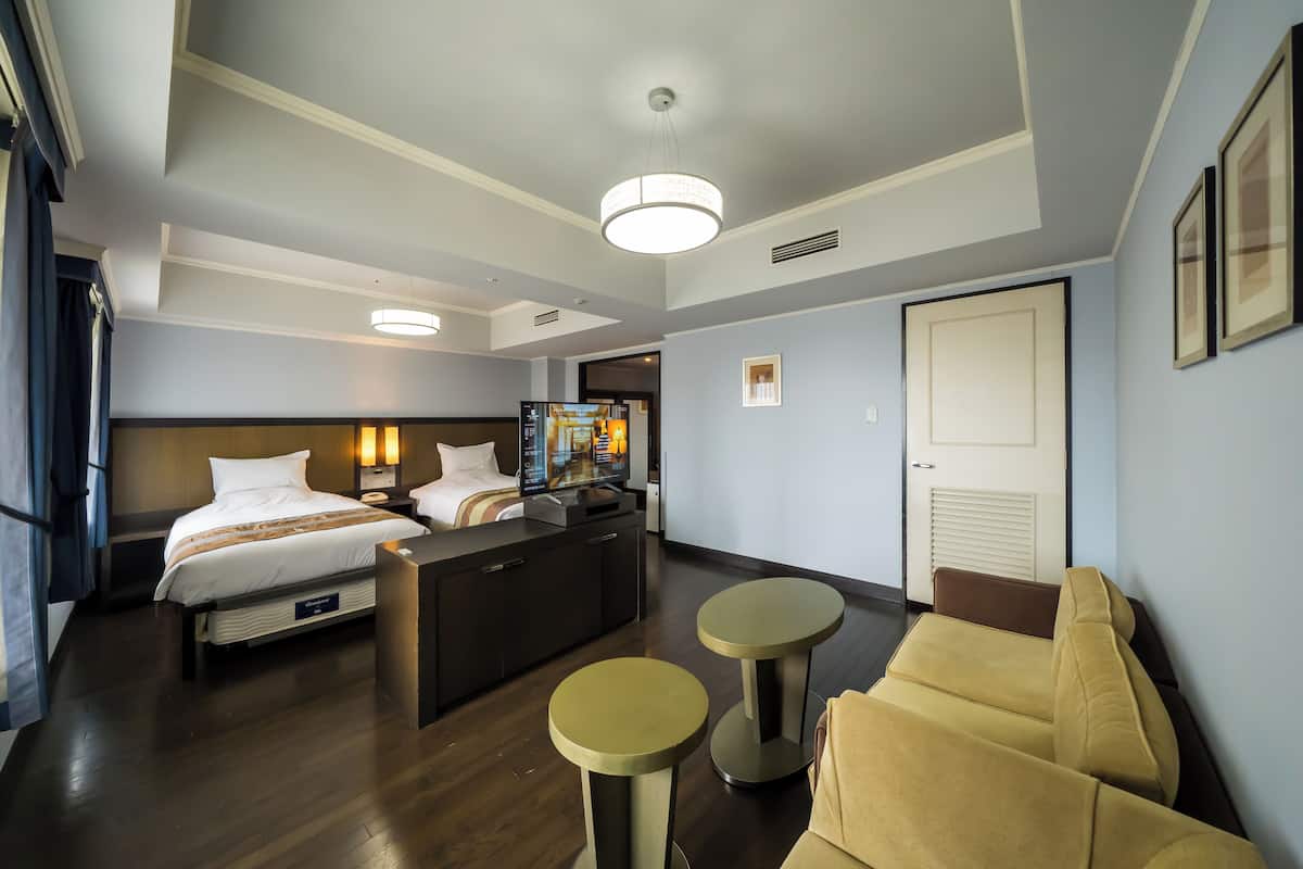 Une chambre d’hôtel comprenant un lit, un bureau, deux petites tables rondes, un canapé et un téléviseur.