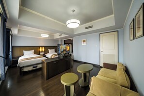 Une chambre d’hôtel comprenant un lit, un bureau, deux petites tables rondes, un canapé et un téléviseur.