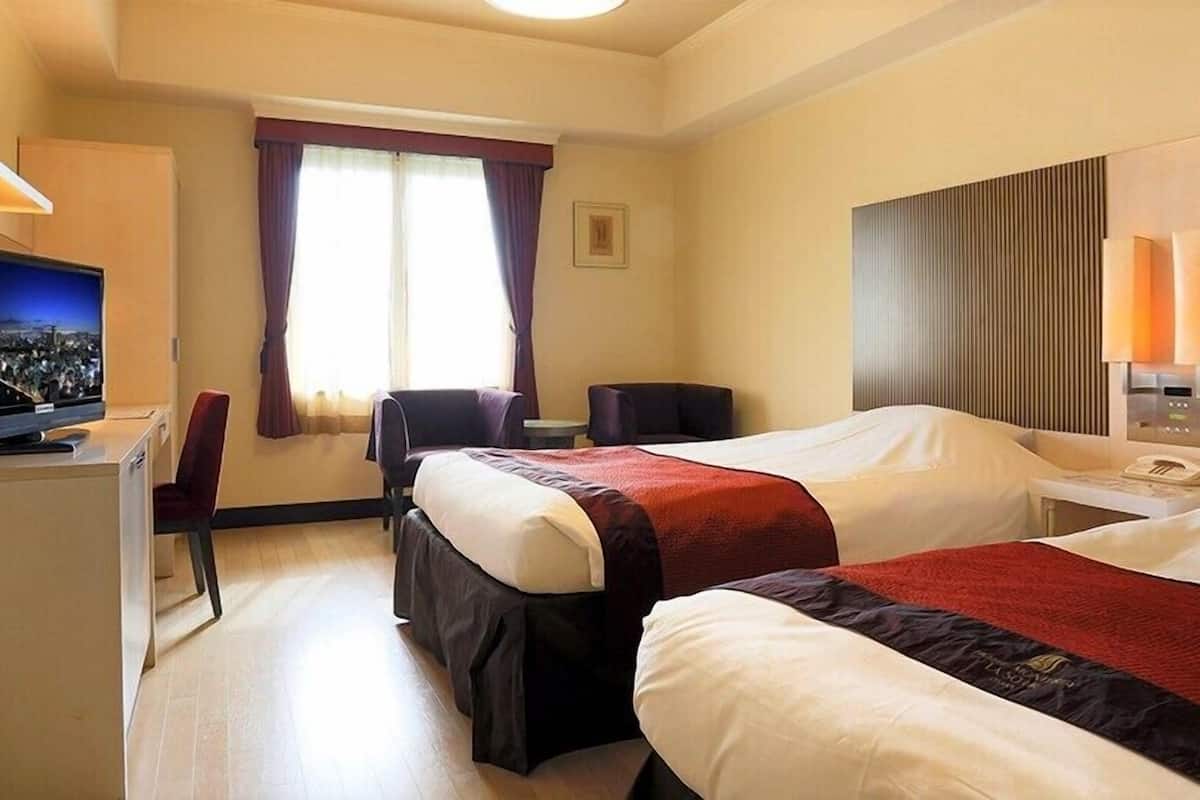 Une chambre d’hôtel avec deux lits, un bureau avec une télévision, une chaise, une fenêtre avec des rideaux et un téléphone fixé au mur.