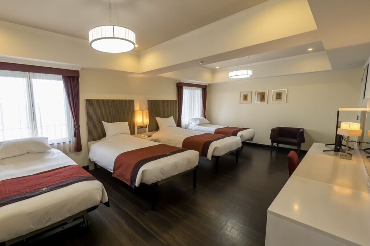 Une chambre d’hôtel avec trois lits, un bureau et une chaise.