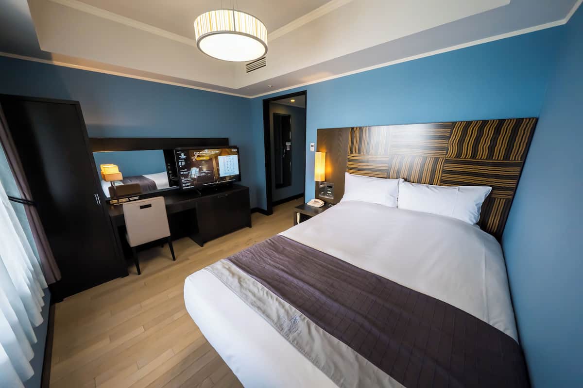 Une chambre d’hôtel avec un grand lit, un bureau équipé d’un ordinateur, une lampe et une tête de lit moderne.