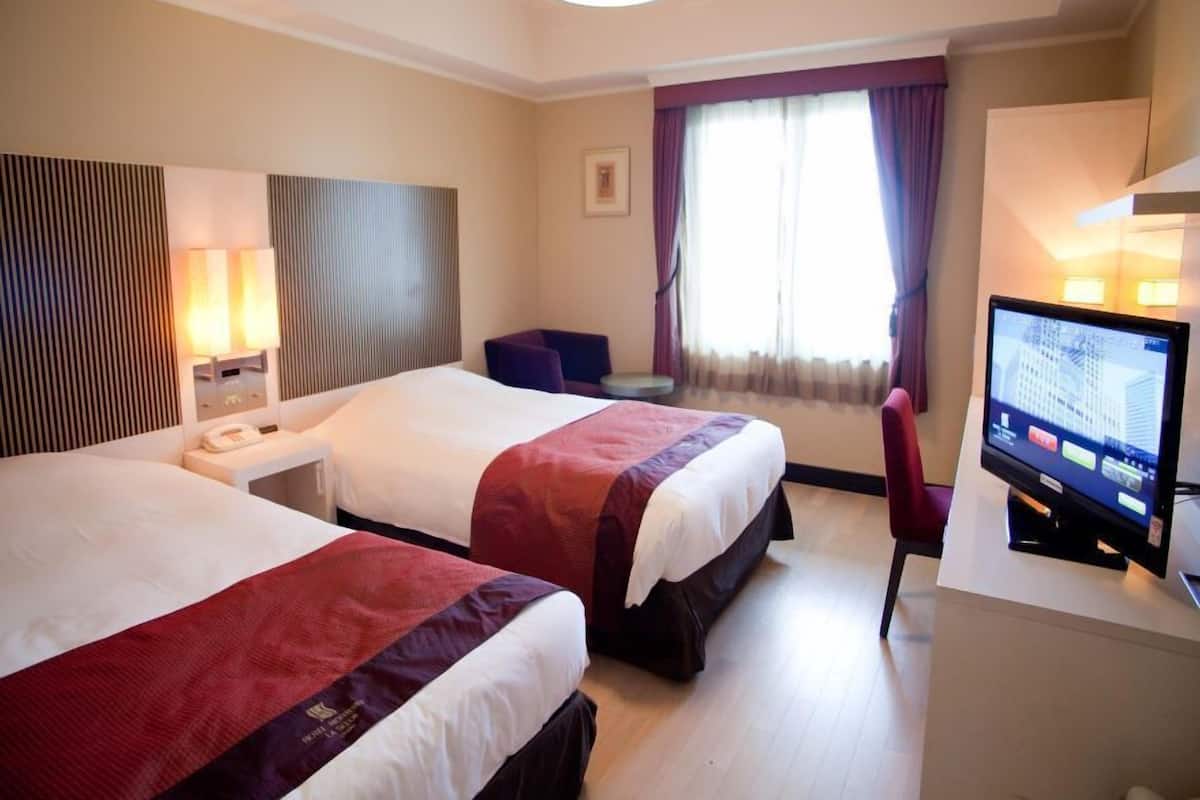 Une chambre d’hôtel avec deux lits, un bureau, une télévision et une fenêtre avec des rideaux.