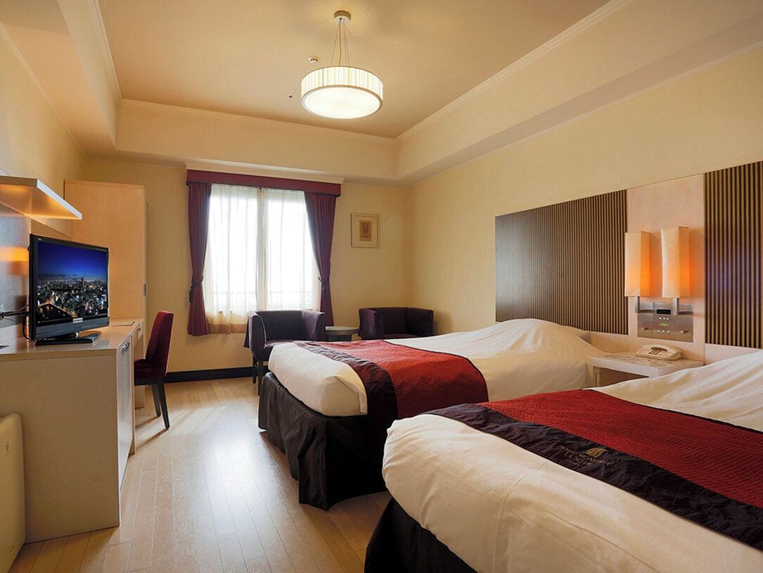 A hotel room with two beds, a desk with a computer, a chair, a TV, and a window with curtains.