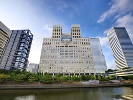 A modern hotel with a central atrium, surrounded by high-rise buildings, and a river in the foreground.
