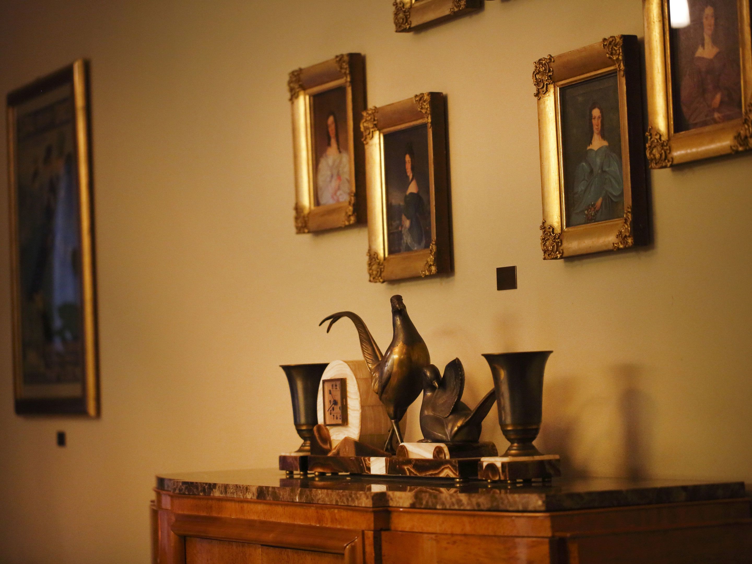 A wall with framed portraits and a marble countertop with a clock and decorative items.