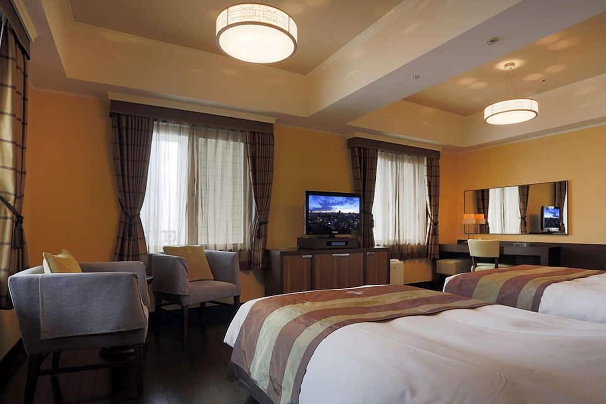 Une chambre d’hôtel avec deux lits, un bureau avec une télévision et un coin salon avec des fauteuils.