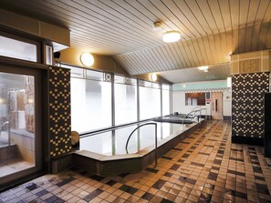 Un espace de bains public doté d’une longue et étroite piscine, de murs carrelés et d’un sol à motifs en damier.