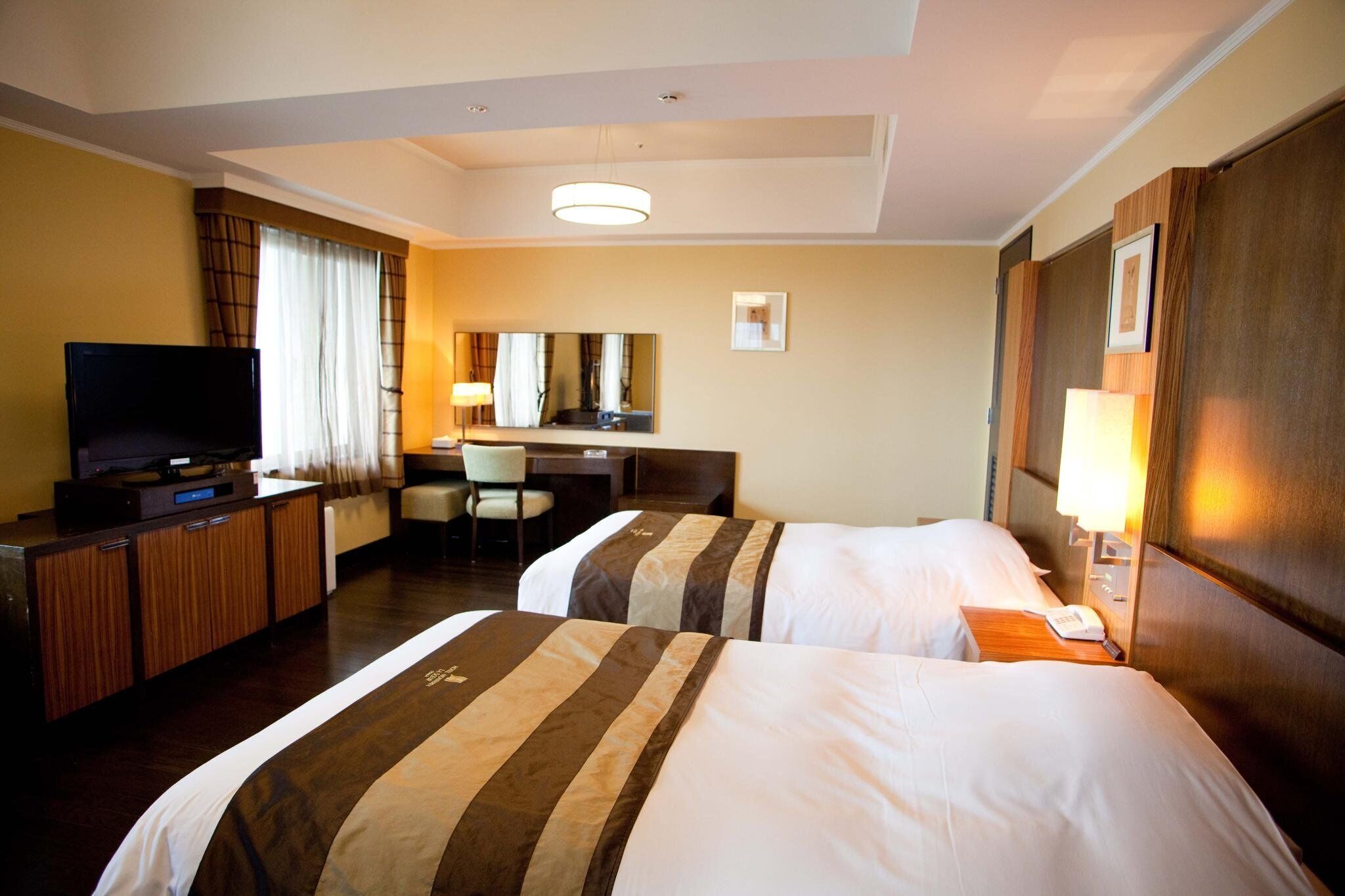 A hotel room with two beds, a desk, a television, and a mirror.