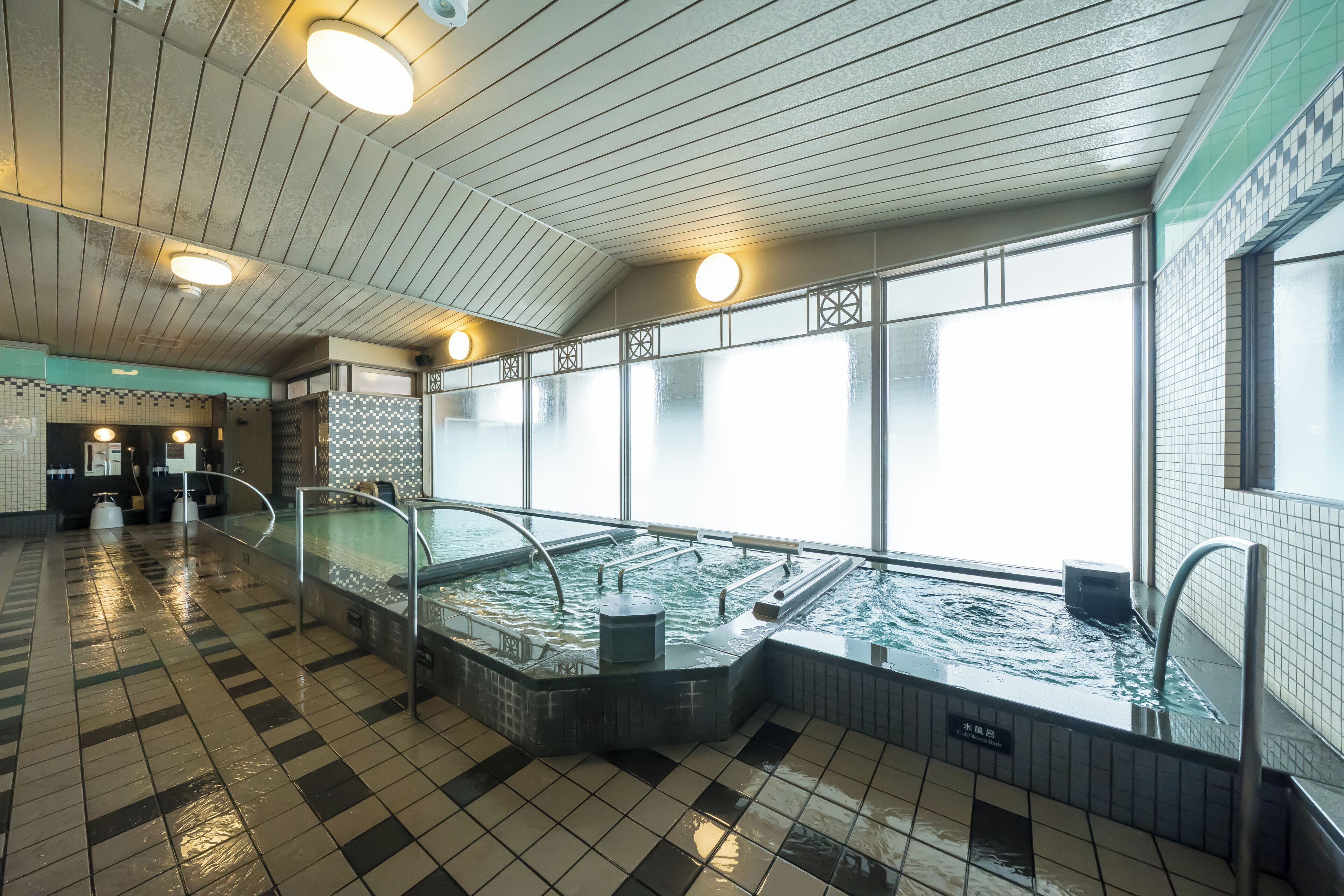 A large indoor swimming pool with a checkered floor, a tiled wall, and a ceiling with linear lighting fixtures.