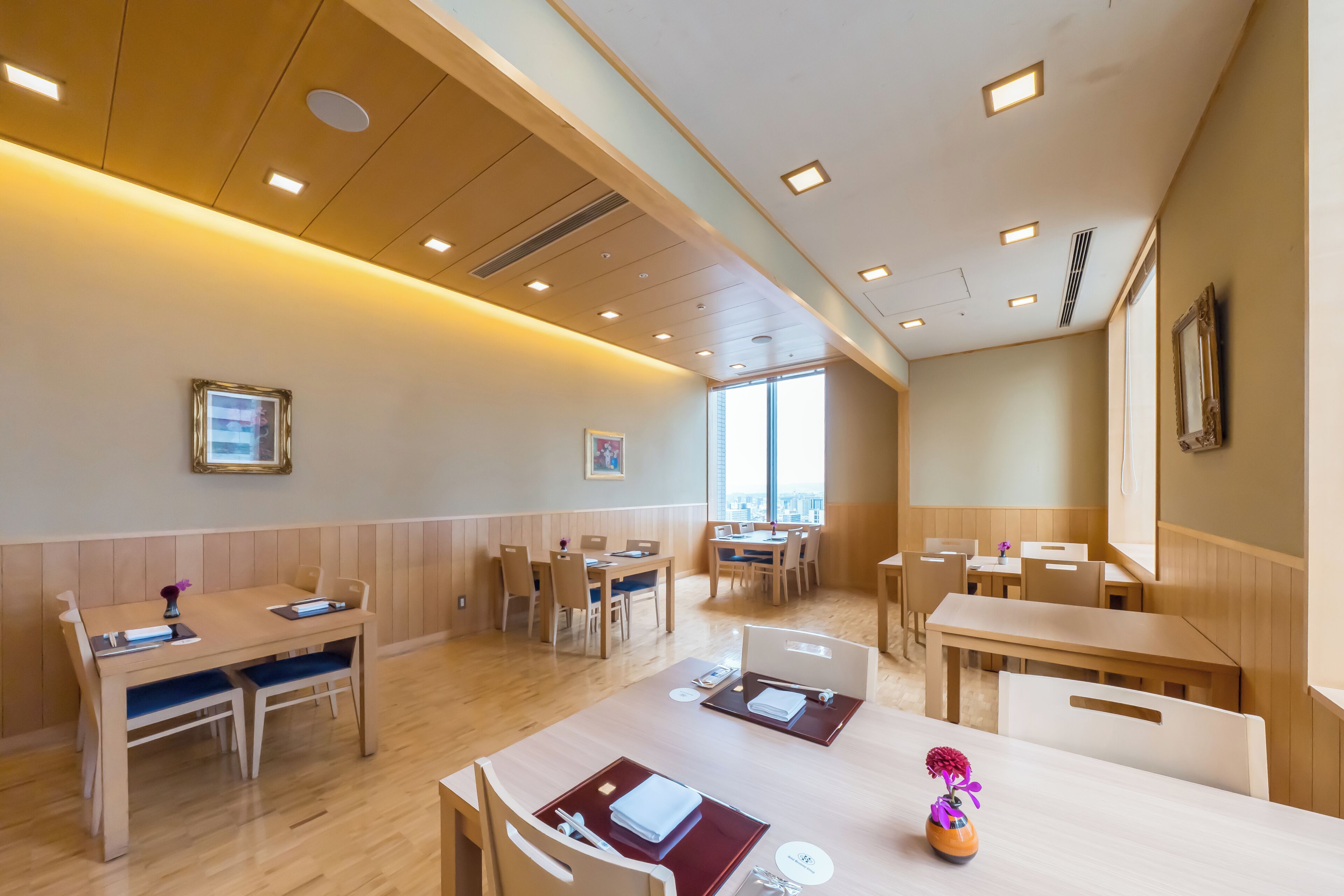 A hotel room with wooden furniture, a large window, and a ceiling with recessed lighting.