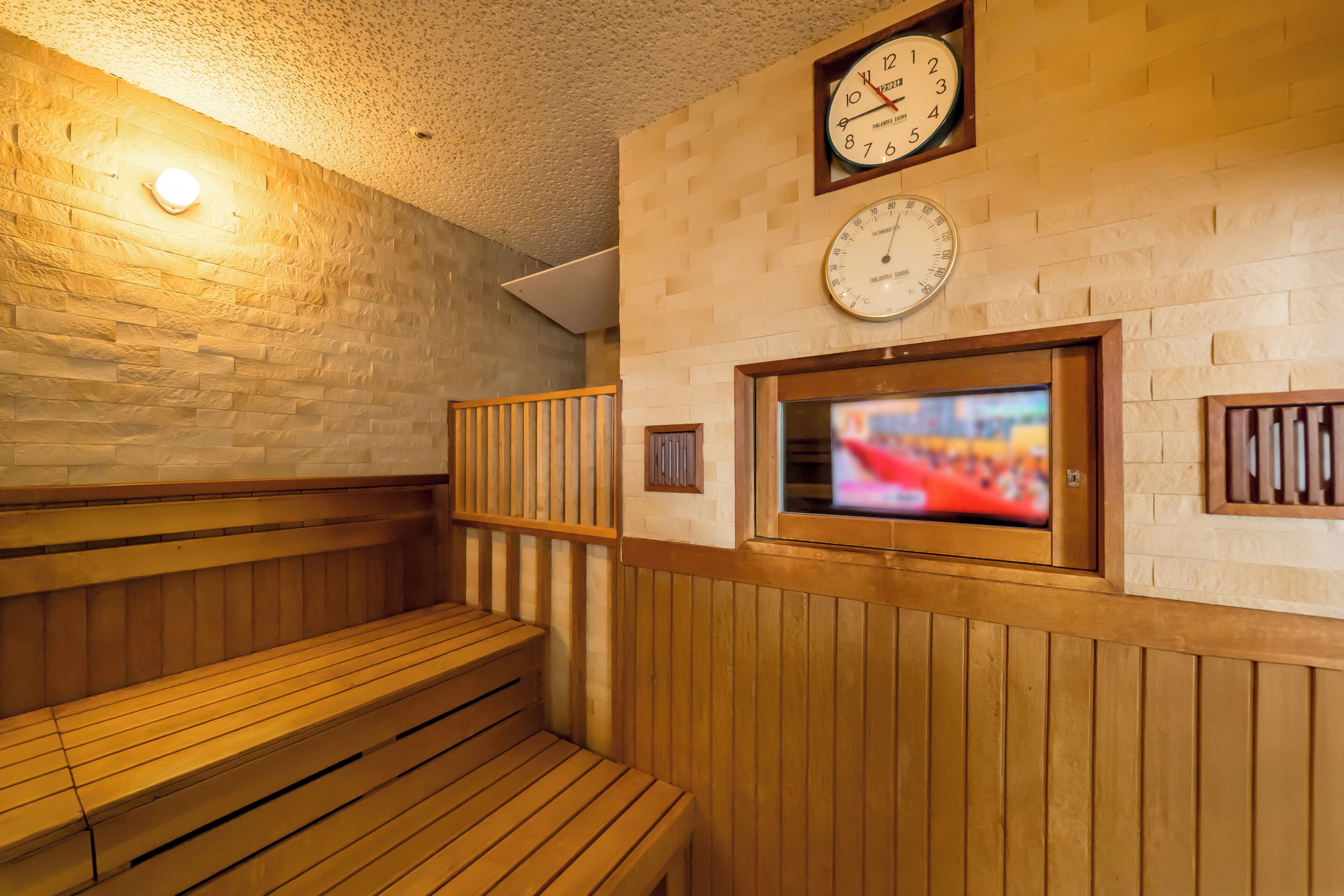 Una sauna con bancos de madera, un reloj en la pared y una pantalla de televisión.