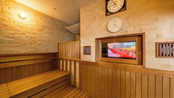 Una sauna con bancos de madera, un reloj en la pared y una pantalla de televisión.