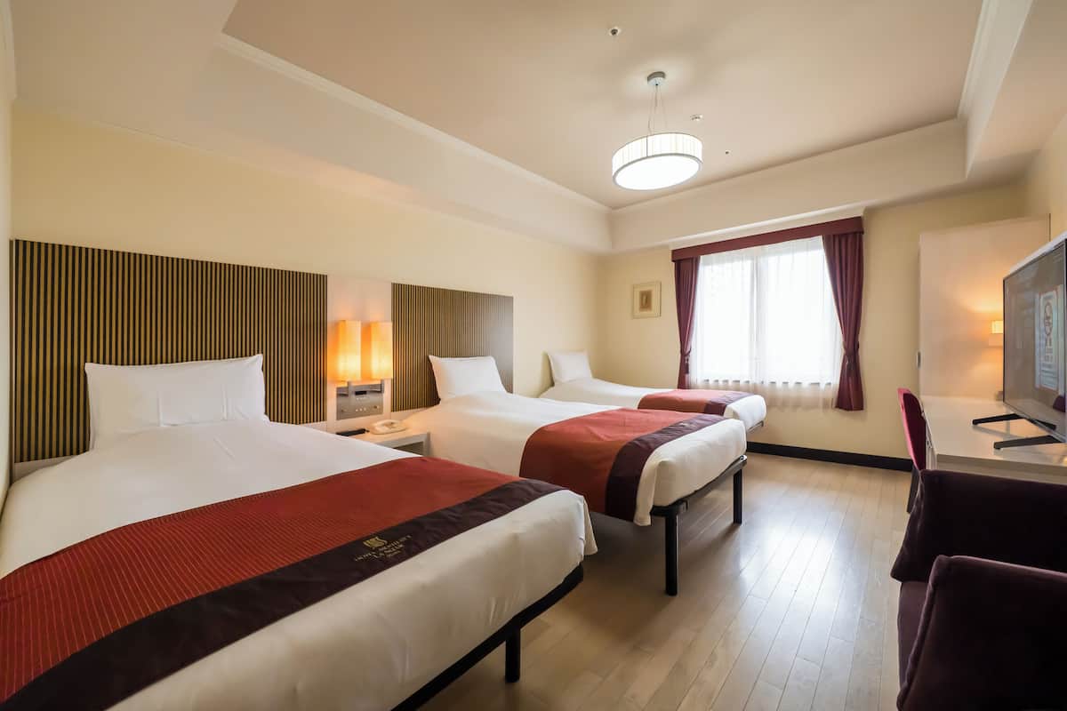 Une chambre d’hôtel avec deux lits, un bureau avec une télévision, une chaise et une fenêtre avec des rideaux.