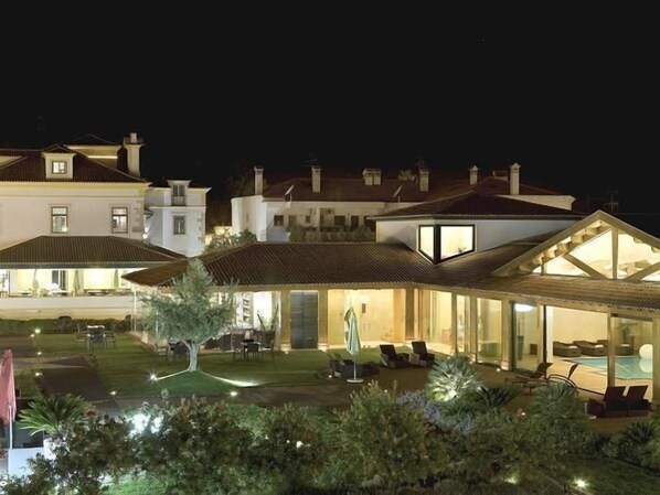 Un espacio exterior bien iluminado con piscina, sillas de descanso y sombrillas.