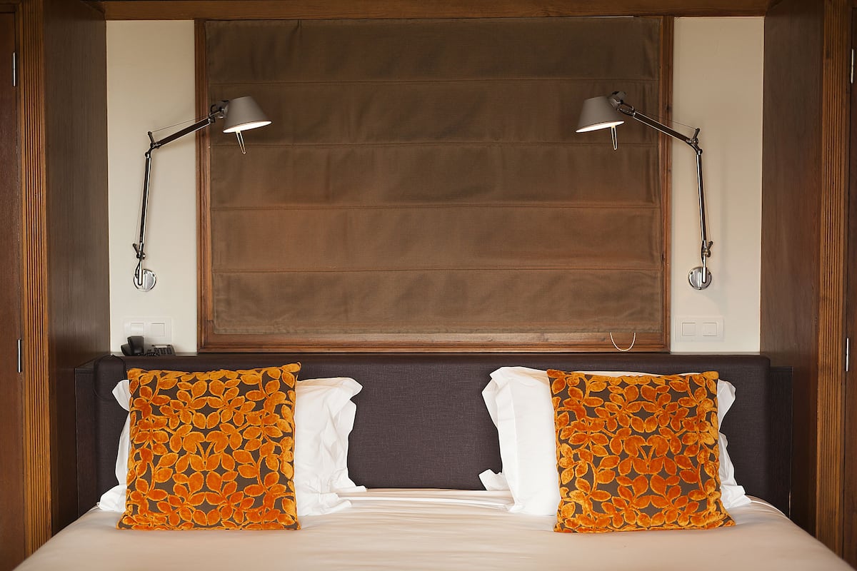 Une chambre d’hôtel avec un lit, deux lampes de chevet et une grande fenêtre avec des stores.
