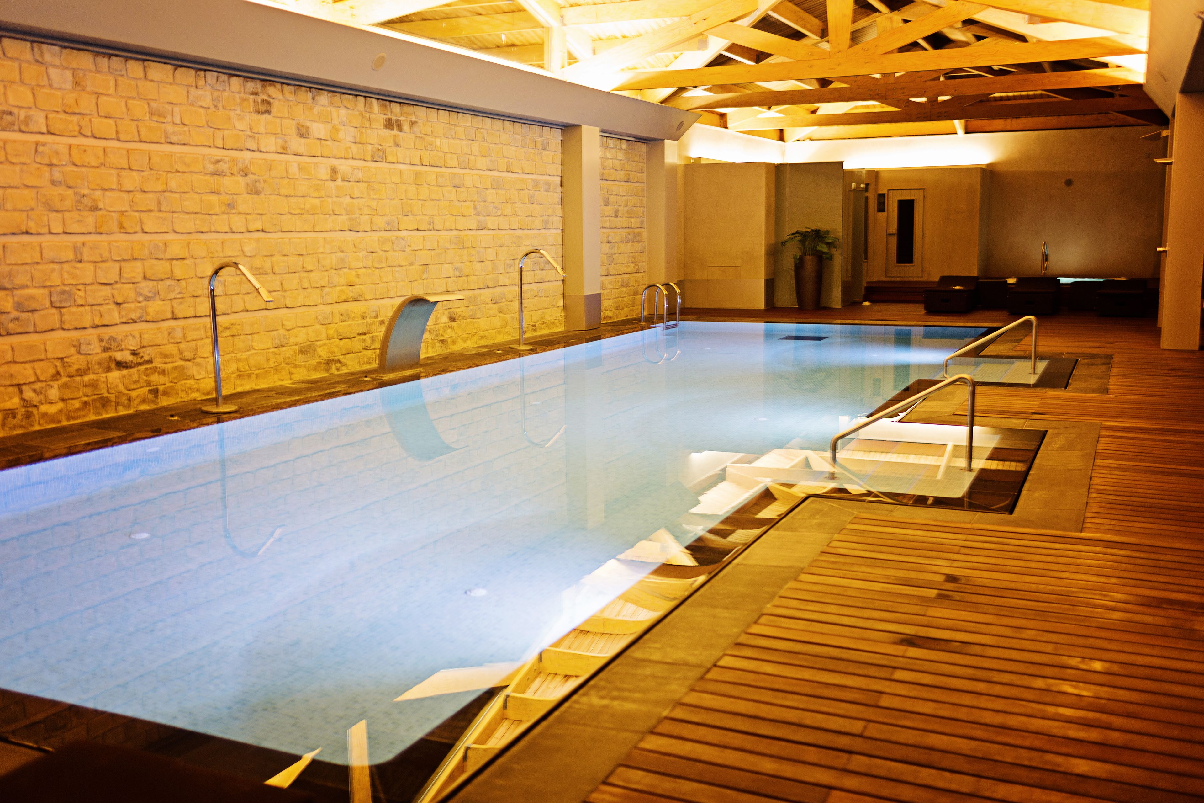 Piscina con suelo de madera y paredes de ladrillo, equipada con escaleras metálicas.