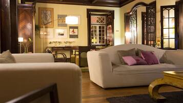 Una sala de estar acogedora con un sofá, sillones y una mesa de centro. El suelo es de madera, hay una lámpara y un cuadro en la pared.