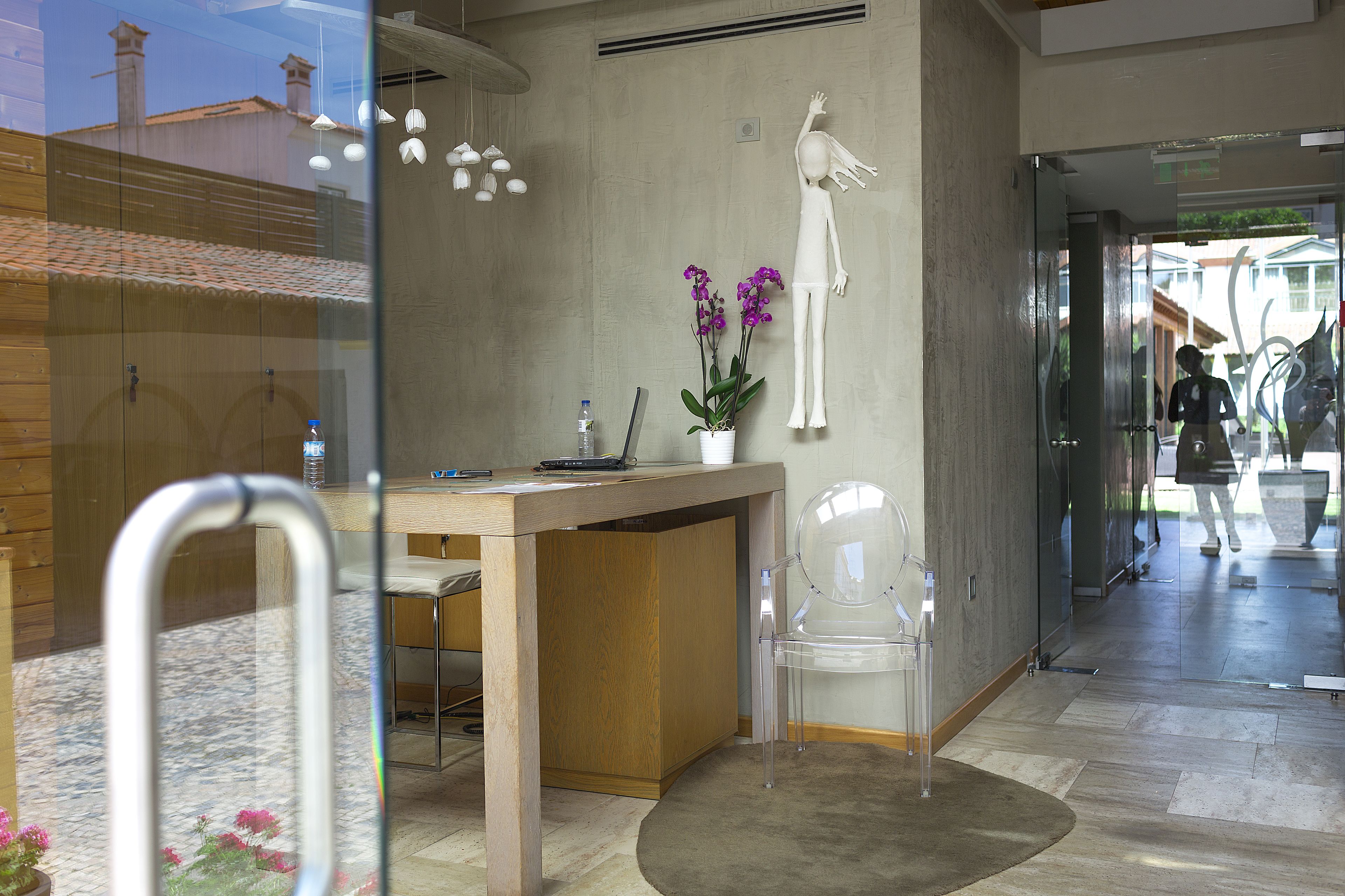Una recepción con un mostrador de madera, una silla de plástico transparente y una orquídea en maceta.