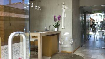 Una recepción con un mostrador de madera, una silla de plástico transparente y una orquídea en maceta.