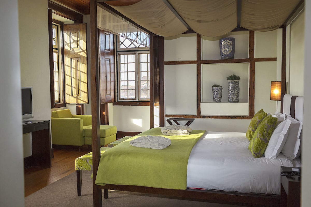 Une chambre bien éclairée, avec un lit, un bureau et une chaise. Elle est dotée de fenêtres qui laissent entrer la lumière naturelle, ainsi que d’une étagère où sont disposés des objets décoratifs.